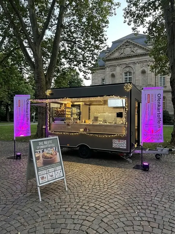 Shepherd's Delight Foodtrailer abends beleuchtet bei einer Veranstaltung, mit Ofenkartoffel-Fahnen und Speisetafel