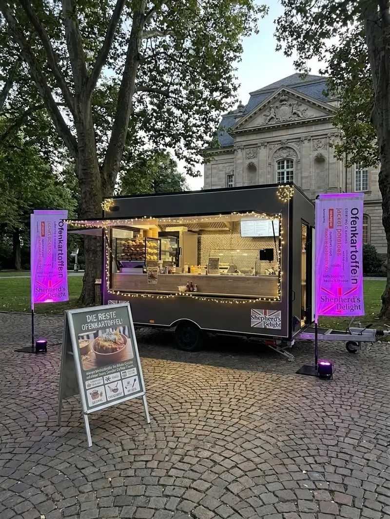 Shepherd’s Delight Foodtrailer abends beleuchtet bei einer Veranstaltung, mit Ofenkartoffel-Fahnen und Speisetafel