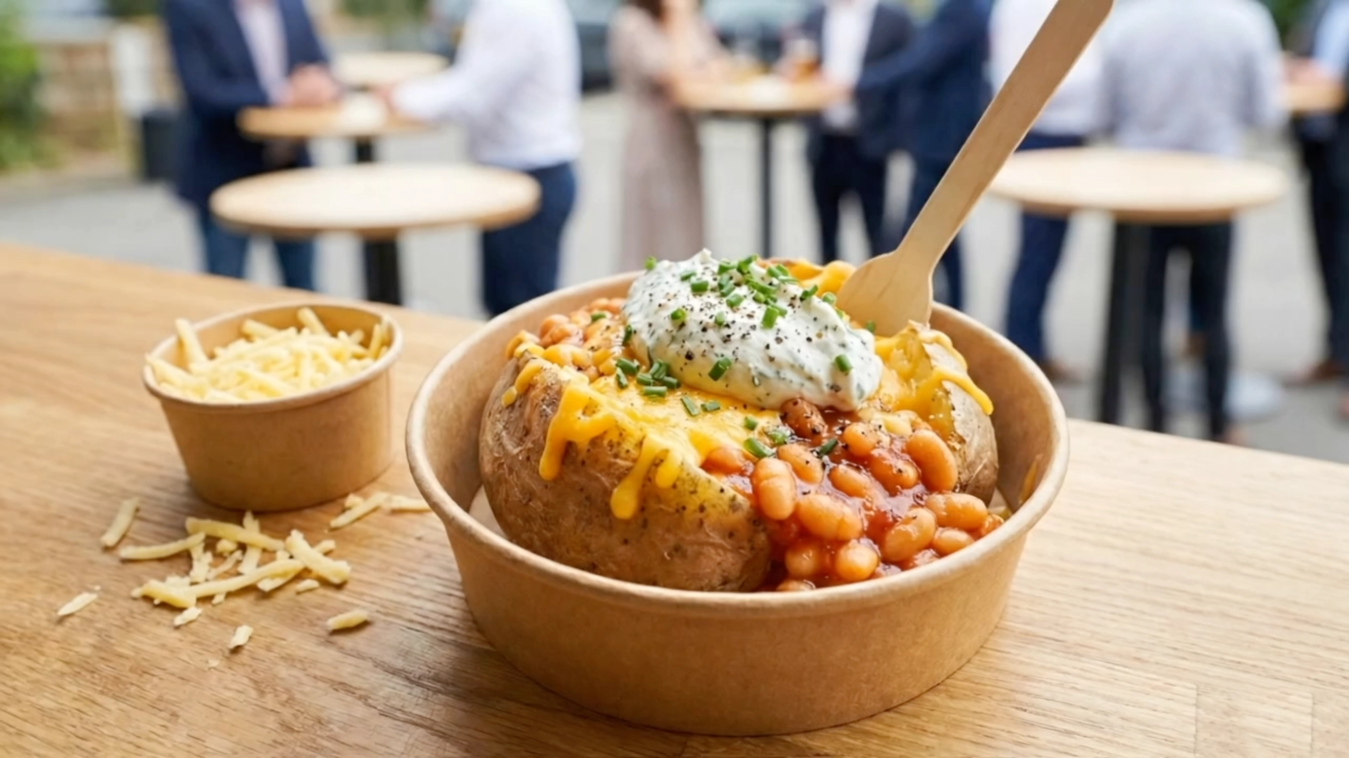Ofenkartoffel mit Baked Beans, Cheddar und Sour Cream auf einem Stehtisch