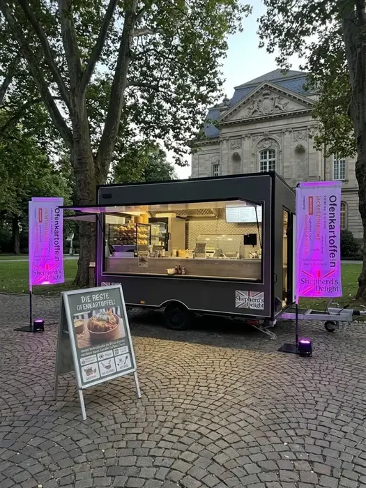 Beleuchteter Foodtrailer bei Dämmerung vor historischer Kulisse